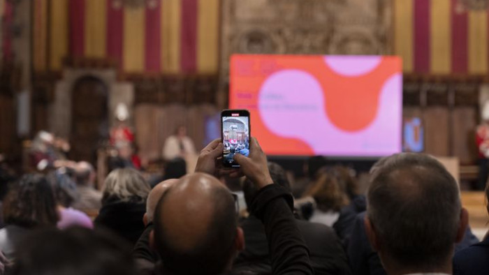 Un home del públic fa un vídeo amb el telèfon mòbil durant l’acte de presentació de la Biennal Ciutat i Ciència 2022, al Saló de Cent de l’Ajuntament de Barcelona.